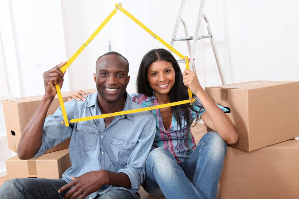 Young smiling couple with moving boxes holding a yellow house shaped cutout